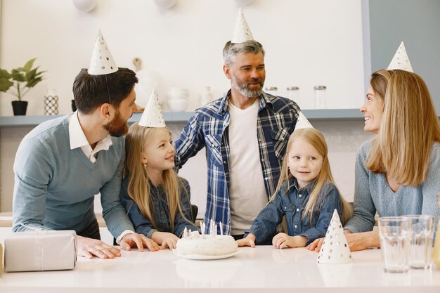 Familie und zwei ihre Töchter haben eine Feier. Auf einem Tisch steht ein Kuchen mit Kerzen.