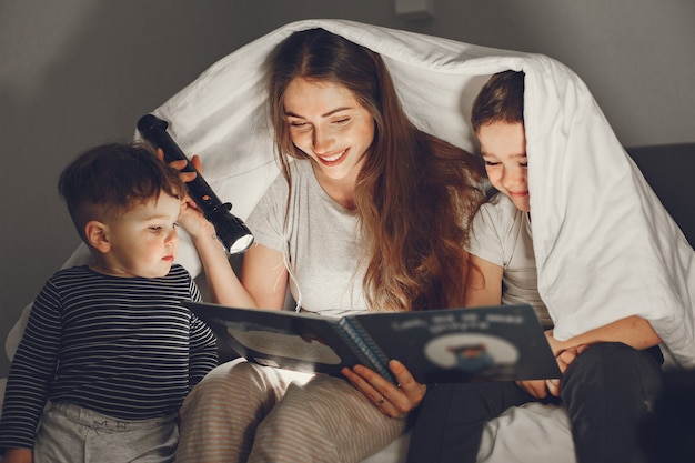 Familie unter der Decke im Bett liest ein Buch.