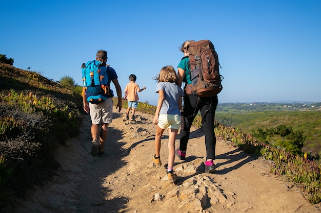 Familie von Reisenden mit Rucksäcken auf der Strecke. Eltern und zwei Kinder wandern im Freien. Rückansicht. Konzept für aktiven Lebensstil oder Abenteuertourismus