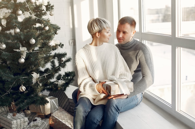 Familie zu Hause. Paar in der Nähe von Weihnachtsdekorationen. Frau in einem grauen Pullover.