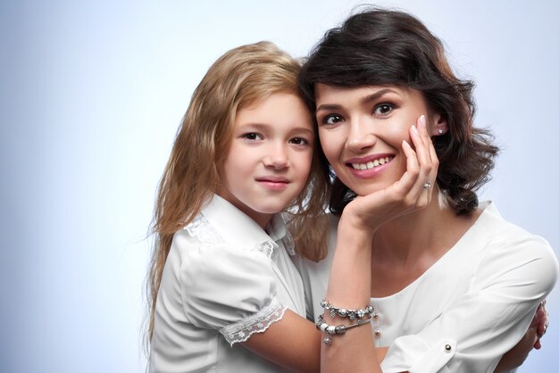 Familienfoto eines glücklichen Paares: Lächeln einer Mutter und ihrer geliebten Tochter. Sie sind sehr hübsch und nett. Sie waren weiße T-Shirts und umarmen sich.