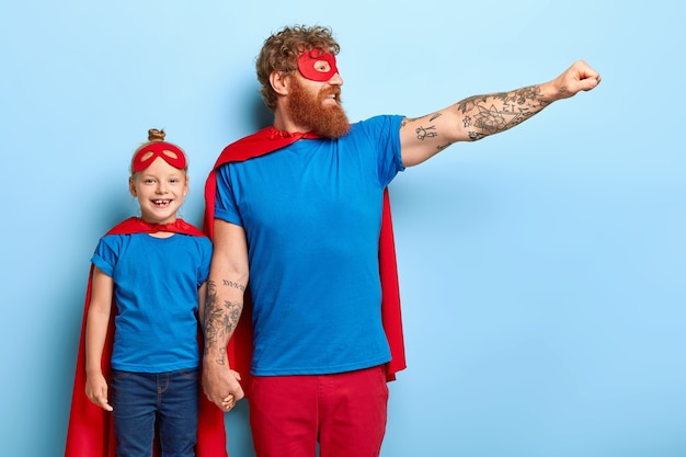 Familienmachtkonzept. Zuversichtlich fröhlicher Vater und kleine Tochter geben vor, Superhelden zu sein