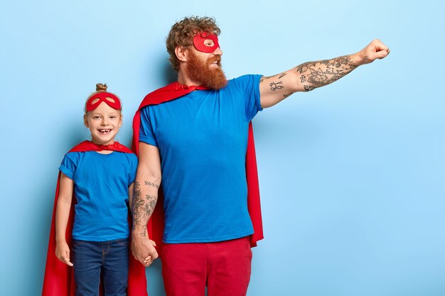 Familienmachtkonzept. Zuversichtlich fröhlicher Vater und kleine Tochter geben vor, Superhelden zu sein