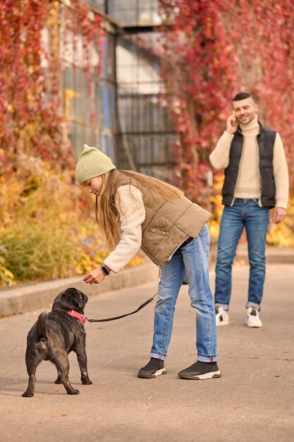 Familienmorgen. Ein Mädchen geht mit einem Hund spazieren, ihr Vater telefoniert