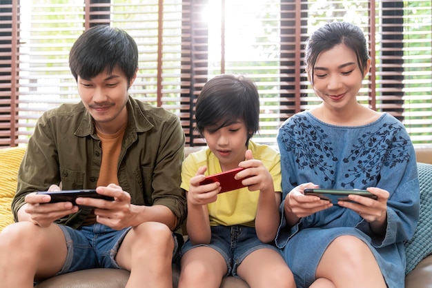 Familienqualität timeasian eltern und sohn sitzen entspannen beim spielen einer spielkonsole oder schlau lachen zusammen fröhlich lächelnd auf der sofacouch im wohnzimmer im homeasian family homs isolation quarantäne ideenkonzept