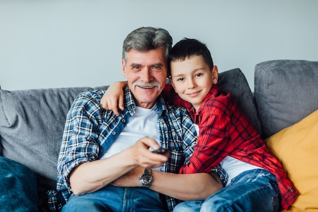 Familienzeit. Fröhlicher Enkel umarmt mit seinem Großvater. Wohnzimmer.