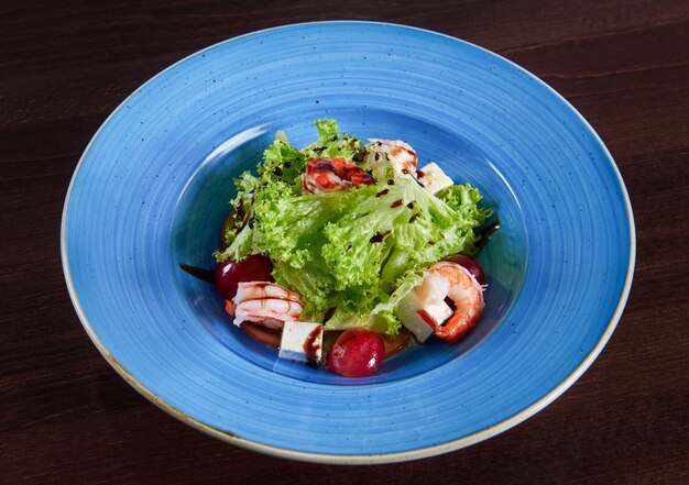 Fantastischer köstlicher garnelensalat mit feta-käse und trauben serviert in einer großen blauen rustikalen platte draufsicht