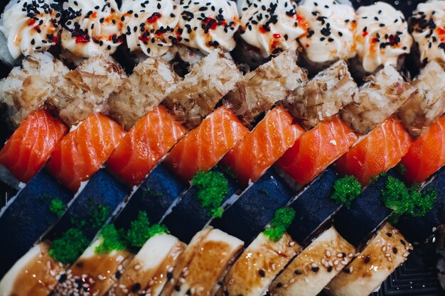 Farbenfrohes, köstliches Sushi-Set, das auf dem Teller liegt, einschließlich verschiedener Zutaten, Fisch, Kaviar, Reis, Gurke, Lachs, Sojasauce, Wasabi, Sesamsamen. Eine interessante Präsentation