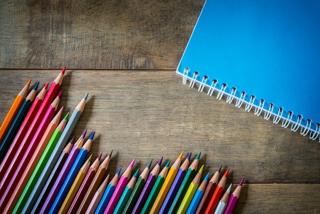 Farbige Bleistifte und Notizbuch auf Holz