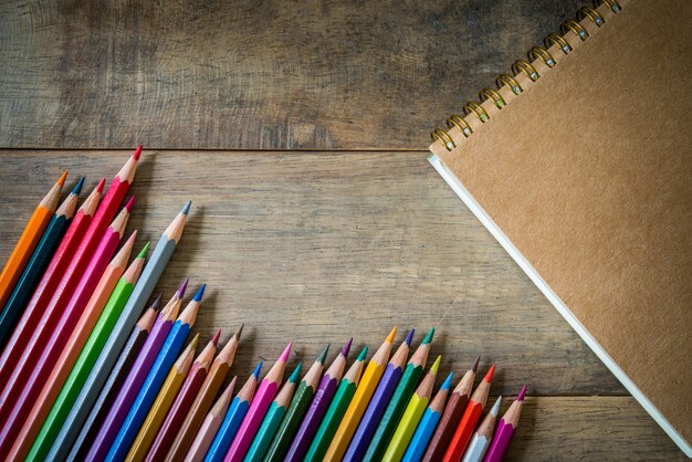 Farbige Bleistifte und Notizbuch auf Holz