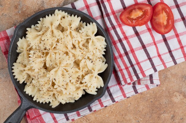 Farfalle auf schwarzer Pfanne mit Tomatenscheiben.