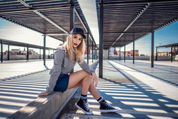 Fashion Hipster Frau sitzt auf Beton Wand tragen Sneakers