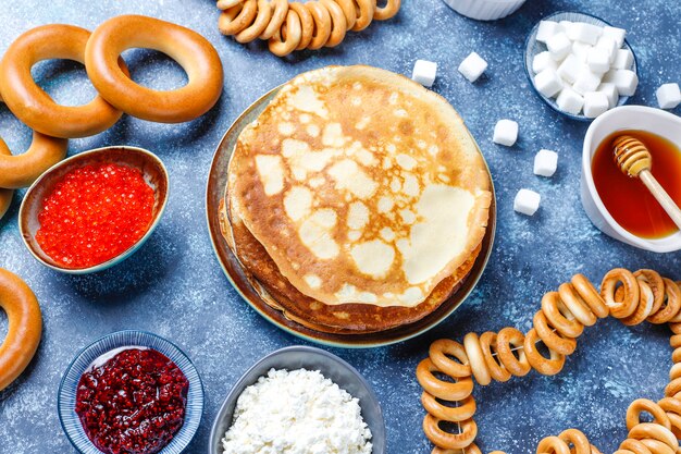 Fastnacht Maslenitsa Festival Mahlzeit. Russischer Pfannkuchen-Blini mit Himbeermarmelade, Honig, frischer Sahne und rotem Kaviar, Zuckerwürfeln, Hüttenkäse im Dunkeln