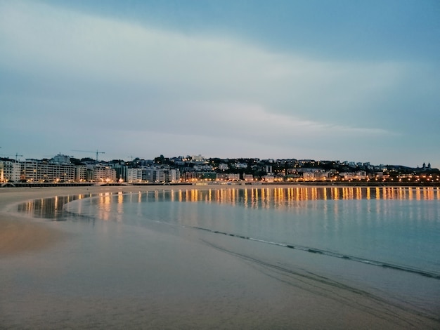 Faszinierende Abendlandschaft der Stadtlichter, die im Ozean in San Sebastian, Spanien reflektieren