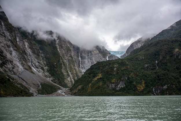 Faszinierende Aussicht auf das ruhige Meer und die felsigen Berge mit Wasserfall