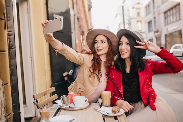 Faszinierende Ingwerfrau, die Selfie im Straßencafé mit ihrem Freund macht