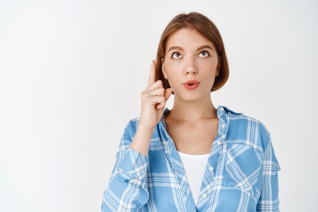 Kostenloses Foto faszinierte junge mädchen sagen wow und zeigen mit neugierigem gesicht nach oben, das interessante promo-angebote vor weißem hintergrund zeigt