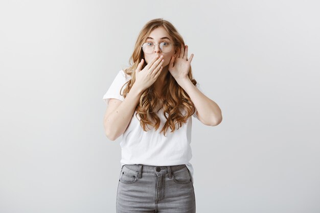 Fasziniertes blondes Mädchen, das klatscht, lauscht und überrascht aussieht