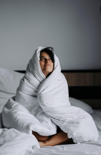 Faule Frau, eingewickelt in eine weiche Decke, die im gemütlichen Bett sitzt