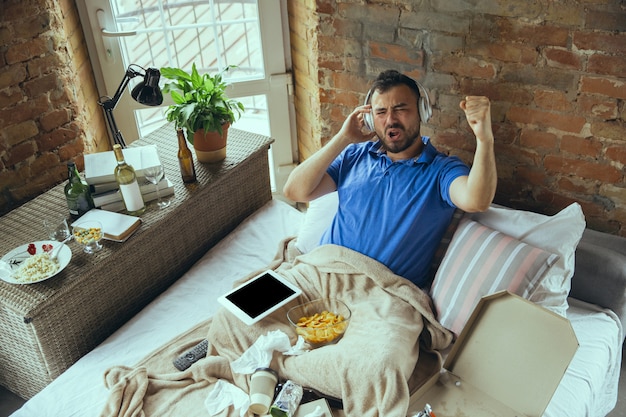 Fauler Mann, der das ganze Leben in seinem Bett lebt, umgeben von Unordnung