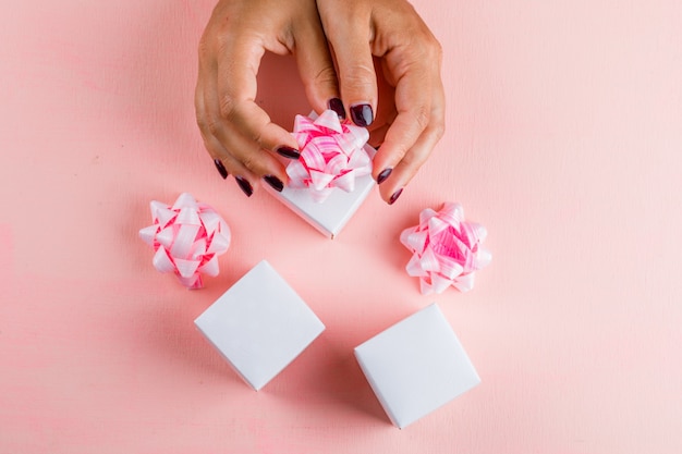 Feierkonzept mit Bandbögen auf rosa Tisch flach legen. Frau, die Geschenkboxen vorbereitet.