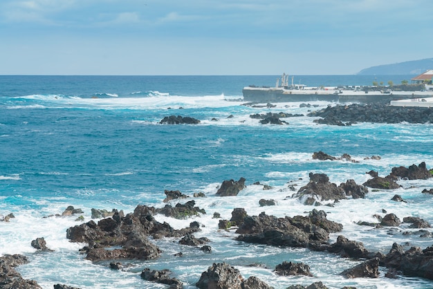 Felsiges Ufer von Puerto de la Cruz. Wellen des Atlantischen Ozeans rollen über den Felsen an einem sonnigen Tag, Teneriffa, Spanien