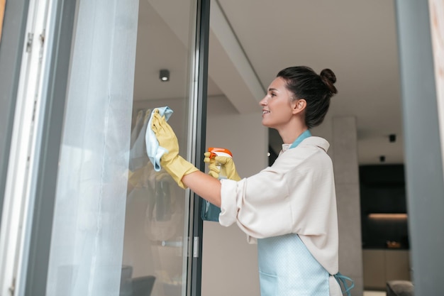 Fenster putzen. Eine Frau in Schürze, die die Fenster putzt und beteiligt aussieht