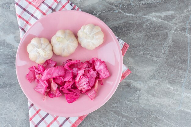 Fermentierter Kohl. Sauerkraut mit eingelegtem Knoblauch auf rosa Teller.