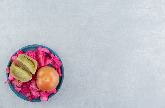 Fermentierter Rotkohl, ganze und in Scheiben geschnittene Tomaten in einer Holzplatte auf der Marmoroberfläche