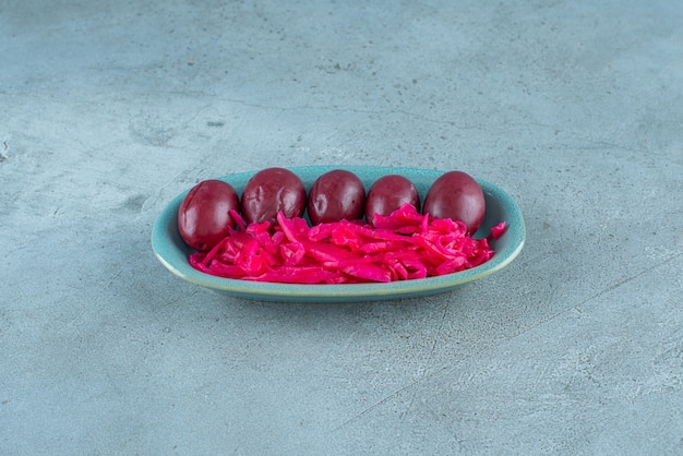 Fermentiertes rotes Sauerkraut mit Pflaumen auf einem Teller auf dem blauen Tisch.