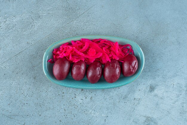 Fermentiertes rotes Sauerkraut mit Pflaumen auf einem Teller auf dem blauen Tisch.