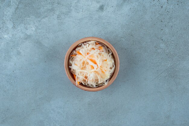 Fermentiertes Sauerkraut mit Karotten in einer Tonschüssel auf dem blauen Tisch.