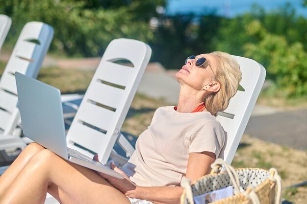 Fernarbeiten. Schöne blonde Frau mit Laptop sitzt in einer Chaiselongue