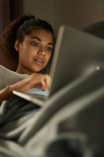 Fernunterricht. Attraktive junge gemischtrassige Studentin, die mit ihrem Laptop studiert, während sie zu Hause auf dem Bett liegt