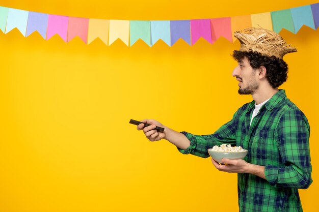 Festa junina junger süßer kerl im brasilianischen festival des strohhutes, das mit popcorn fernsieht