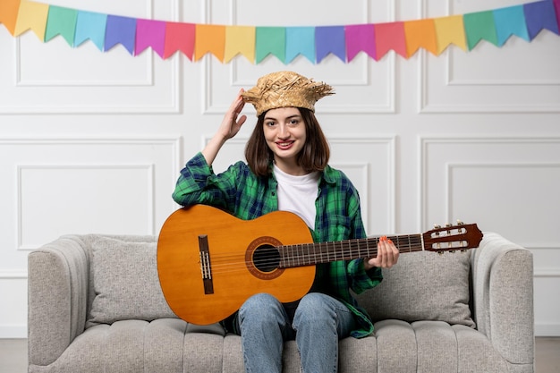 Festa junina süßes, hübsches Mädchen in grünem Strohhut mit bunten Fahnen, die braune Gitarre halten