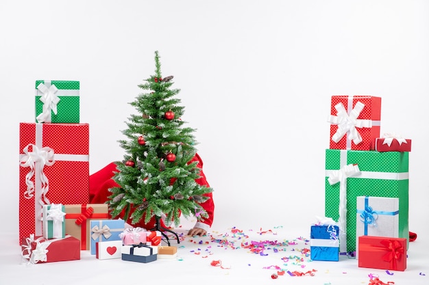 Kostenloses Foto festliche feiertagsstimmung mit weihnachtsmann, der sich hinter geschmücktem weihnachtsbaum auf weißem hintergrund versteckt