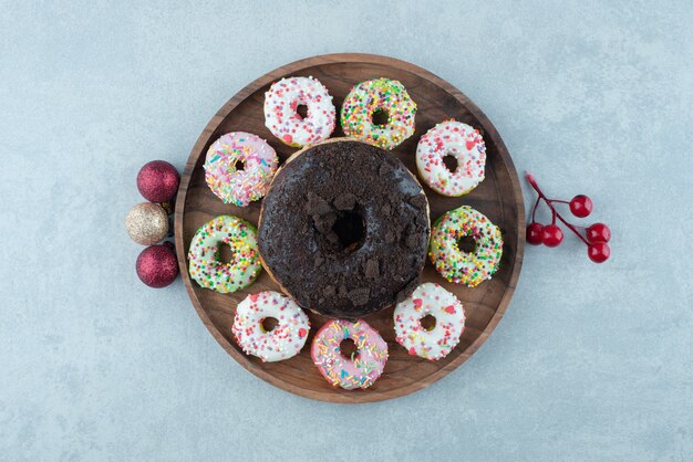 Festliche Ornamente und ein Tablett mit kleinen Donuts um einen einzigen großen Donut auf Marmor.