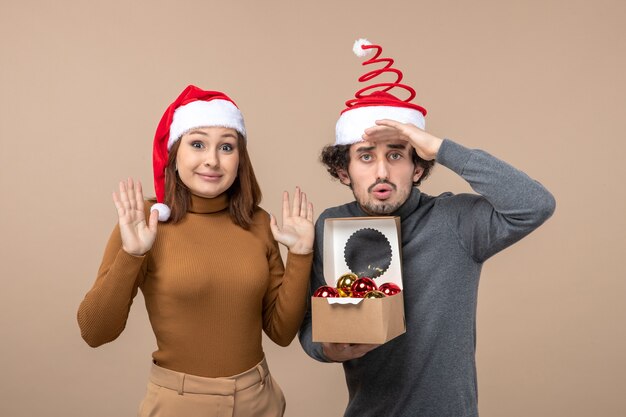 Festliche Stimmung mit aufgeregtem coolem Paar, das rote Weihnachtsmannhüte auf grauem Lagerbild trägt