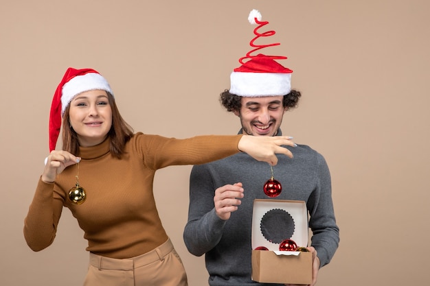 Festliche Stimmung mit aufgeregtem reizendem Paar, das rote Weihnachtsmannhüte trägt, die Dekorationszubehör auf Grau öffnen