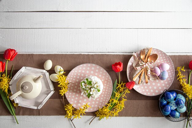 Festlicher Kuchen, Teekanne, Eier und Blumen auf dem Tisch. Osterfeier und Gedeckkonzept.