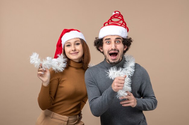 Festliches Konzept der Neujahrsstimmung mit dem kühlen reizenden Paar, das rote Weihnachtsmannhüte auf grauem Bild trägt