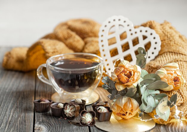 Festliches Stillleben zum Valentinstag mit einem Getränk in einer Tasse, Pralinen und Blumen auf einem unscharfen Hintergrund.