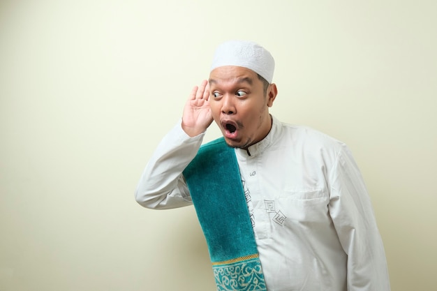 Fetter asiatischer muslimischer mann hört flüstern mit lustigem gesicht zu, neugierig lauscht aufmerksam auf saftigen klatsch