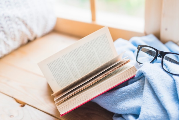 Öffnen Sie Buch und Brillen auf der blauen Decke über dem Tisch