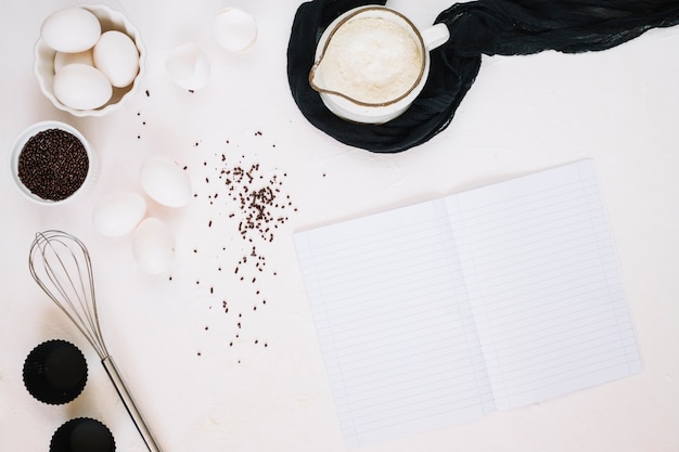 Öffnen Sie das Notebook in der Nähe von Schneebesen und Zutaten