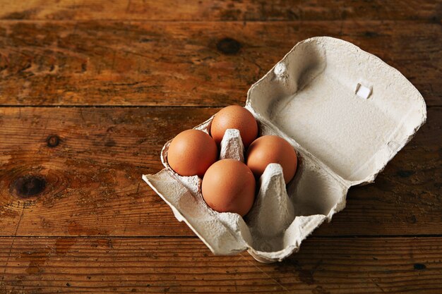 Öffnen Sie den Eierkarton für sechs Eier mit vier braunen Eiern auf einem rauen, rustikalen, braunen Holztisch