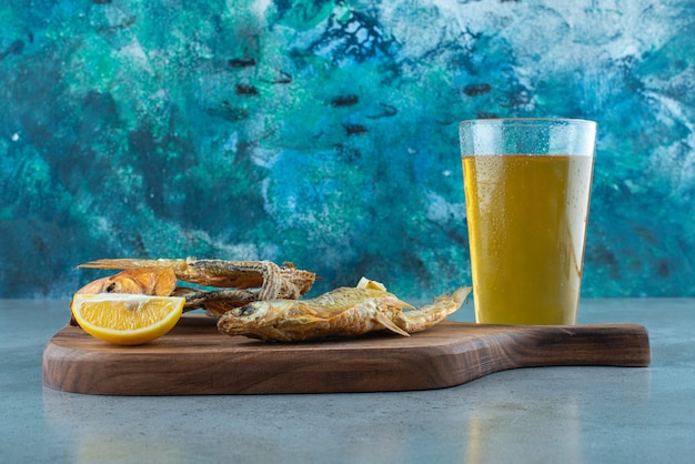 Fisch, Zitronenscheiben und ein Glas Bier an Bord auf Marmor.