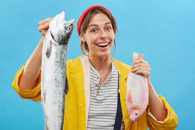 Kostenloses Foto fischerin, die zwei frisch gefangene seefische in ihren händen anbietet