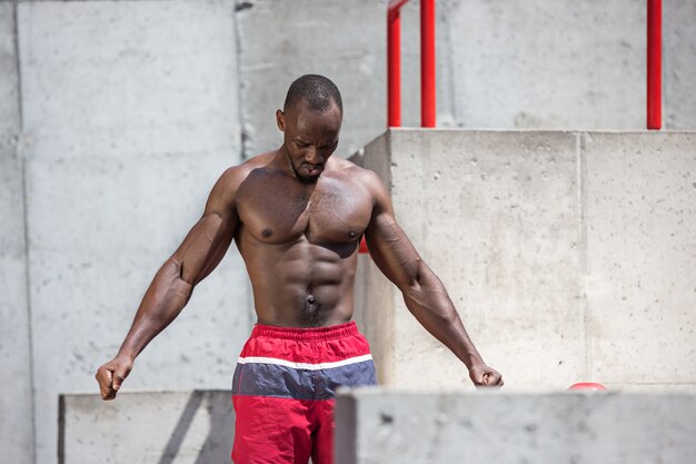 Fit Athlet macht Übungen im Stadion. Afro-Mann im Freien in der Stadt. Sportübungen hochziehen. Fitness-, Gesundheits-, Lifestyle-Konzept